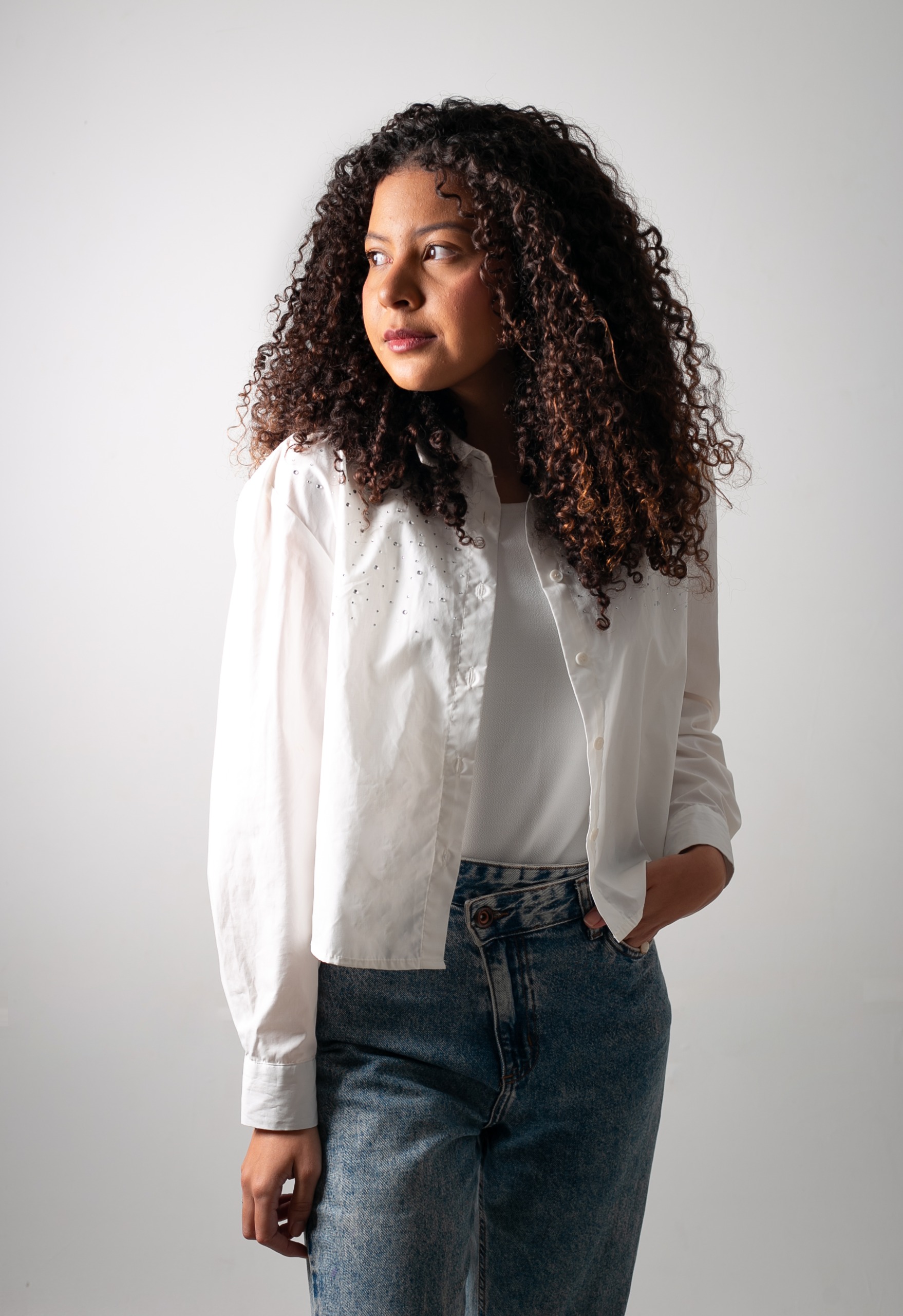 Mulher com camisa branca e jeans, olhando para o lado