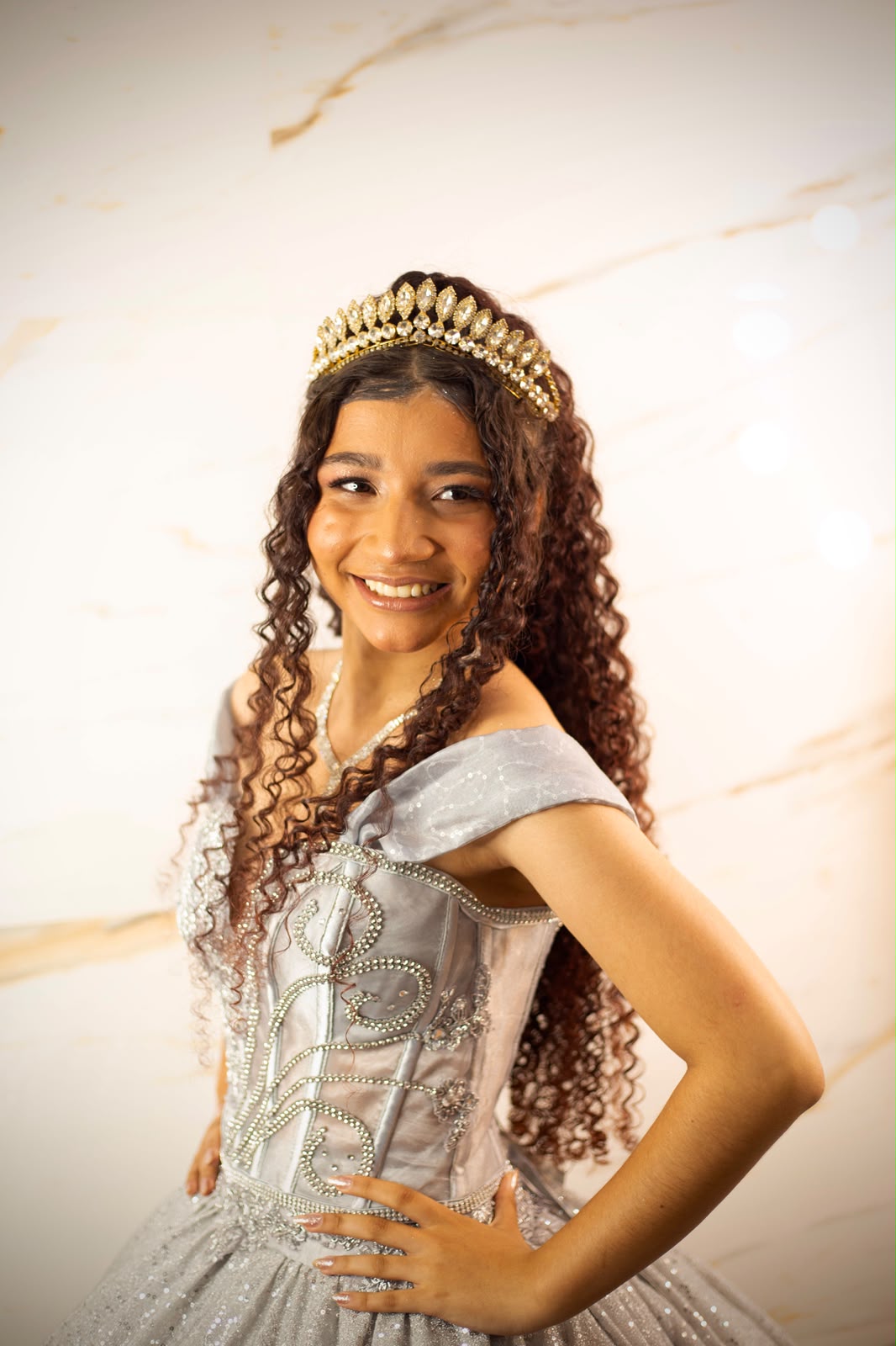 Retrato de debutante sorrindo com coroa e vestido prateado