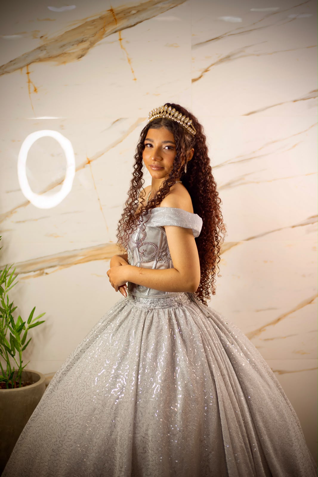 Debutante com coroa e vestido prateado em frente a uma parede de mármore