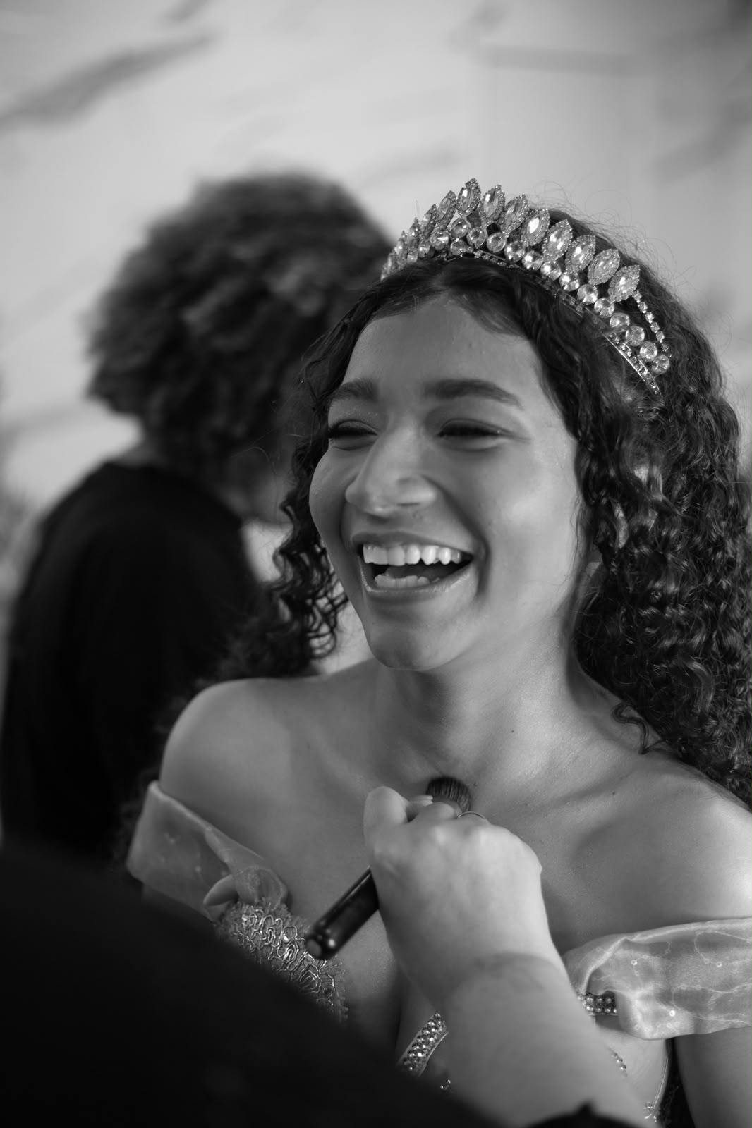 Retrato em preto e branco da debutante sorrindo durante a maquiagem